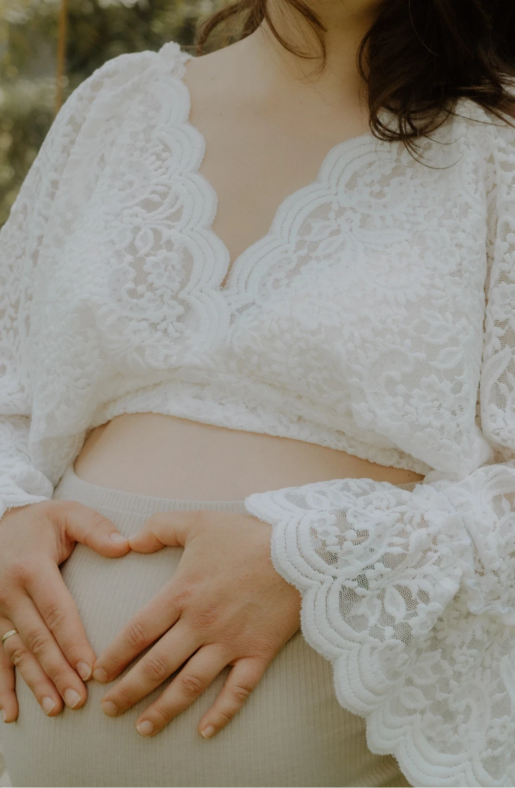 Eine schwangere Frau in einem romantischen Spitzen - Top hat ihre Hände auf ihren Bauch zu einem Herz abgelegt